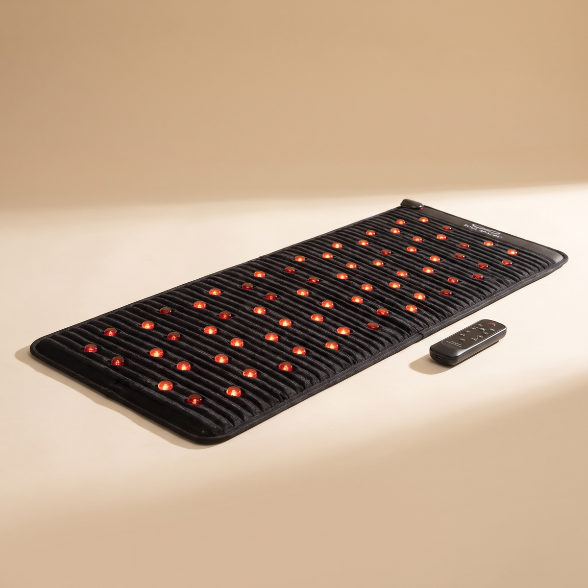 Crystal Recovery PEMF Mat with warm stones glowing, on a cream background with controller